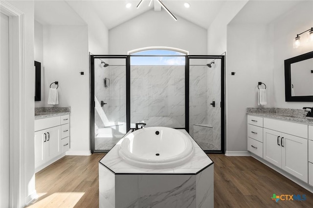 bathroom with a marble finish shower, lofted ceiling, wood finished floors, a garden tub, and a sink