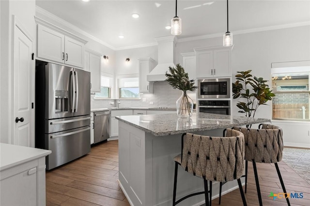 kitchen featuring stainless steel appliances, wood finished floors, tasteful backsplash, a kitchen bar, and custom range hood