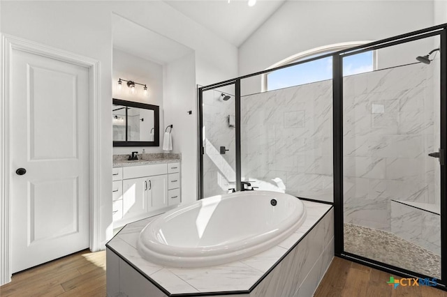 bathroom featuring a garden tub, wood finished floors, vanity, vaulted ceiling, and a marble finish shower