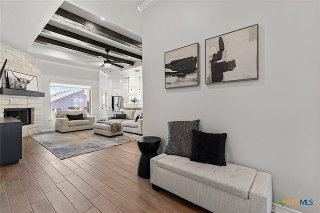 living room with ceiling fan, beam ceiling, wood finished floors, and a stone fireplace