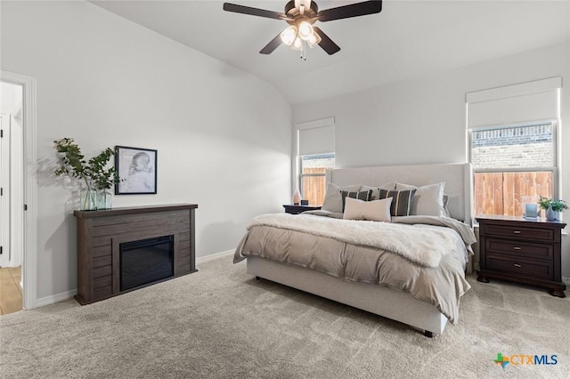 carpeted bedroom with a glass covered fireplace, multiple windows, vaulted ceiling, and baseboards