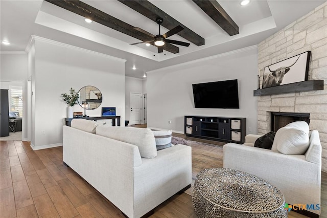 living room featuring beam ceiling, crown molding, a stone fireplace, wood finished floors, and baseboards