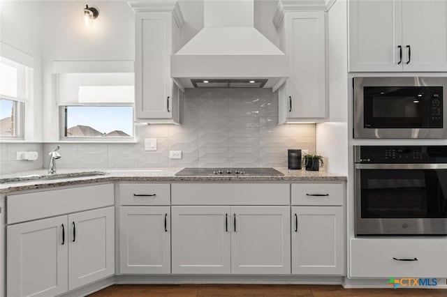 kitchen with black electric stovetop, a sink, built in microwave, oven, and premium range hood