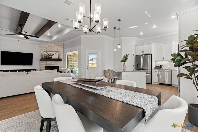 dining space featuring light wood-style floors, beam ceiling, visible vents, and a fireplace