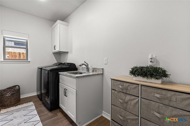 washroom featuring cabinet space, baseboards, dark wood finished floors, washer and dryer, and a sink