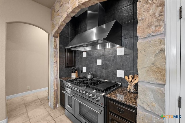 5310 River Oaks Dr, New Braunfels, TX 78132 - kitchen featuring range with two ovens, wall chimney exhaust hood, tasteful backsplash, arched walkways, and dark stone countertops