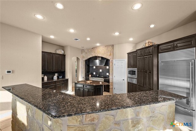 5310 River Oaks Dr, New Braunfels, TX 78132 - kitchen with range with two ovens, wall chimney exhaust hood, a center island with sink, backsplash, and dishwashing machine