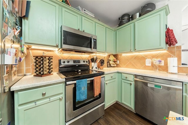 kitchen with decorative backsplash, appliances with stainless steel finishes, green cabinetry, and dark hardwood / wood-style floors