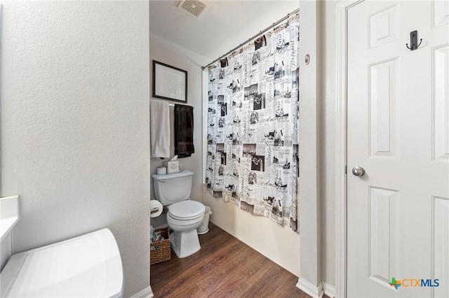 bathroom with toilet, curtained shower, and hardwood / wood-style flooring