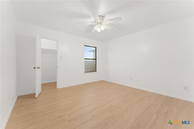 unfurnished bedroom featuring a closet, a spacious closet, light wood-style floors, ceiling fan, and baseboards