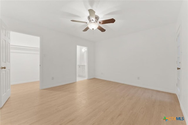 unfurnished bedroom with a walk in closet, a closet, light wood-style flooring, and baseboards