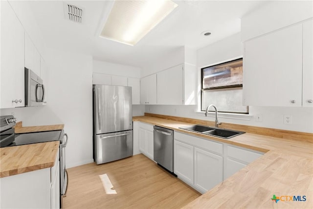 kitchen with visible vents, white cabinets, appliances with stainless steel finishes, wooden counters, and a sink