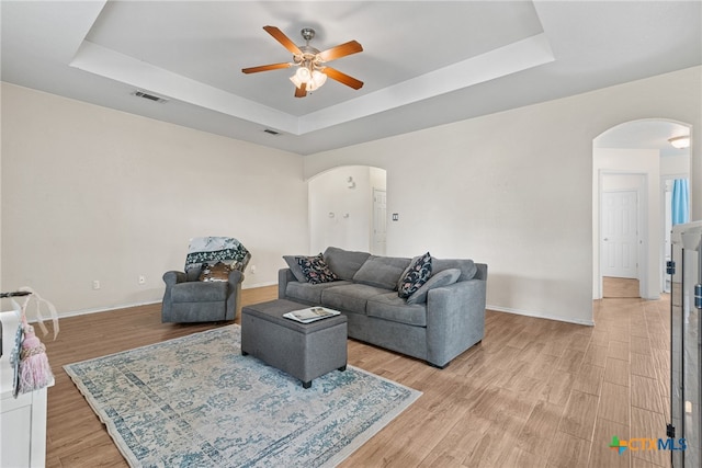 living room featuring light hardwood / wood-style floors, ceiling fan, and a tray ceiling