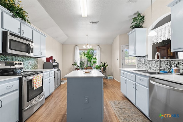 kitchen with stainless steel appliances, sink, pendant lighting, and light wood-type flooring