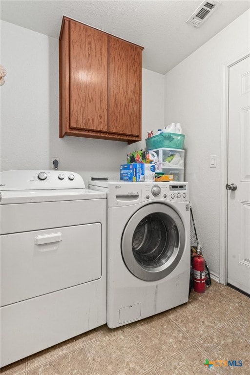 clothes washing area featuring cabinets, washer and dryer, and light tile patterned floors