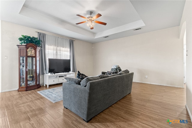 living room with ceiling fan, a raised ceiling, and light hardwood / wood-style flooring