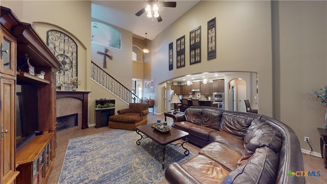 living room with a tiled fireplace, ceiling fan, and high vaulted ceiling