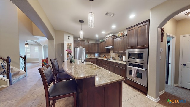 kitchen with dark brown cabinets, light stone counters, stainless steel appliances, and decorative light fixtures