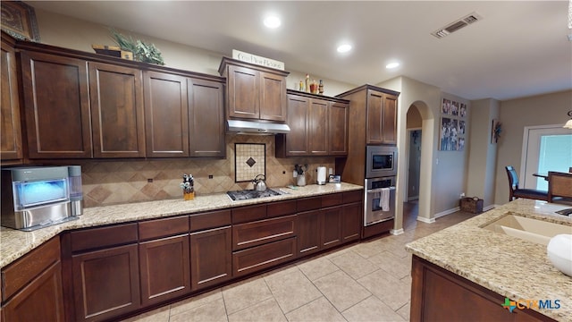 kitchen with light stone countertops, stainless steel appliances, decorative backsplash, dark brown cabinets, and light tile patterned floors