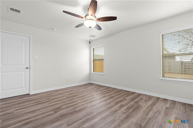 empty room with wood finished floors, visible vents, and baseboards