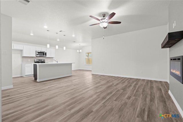 unfurnished living room with ceiling fan, a glass covered fireplace, light wood-style flooring, and baseboards