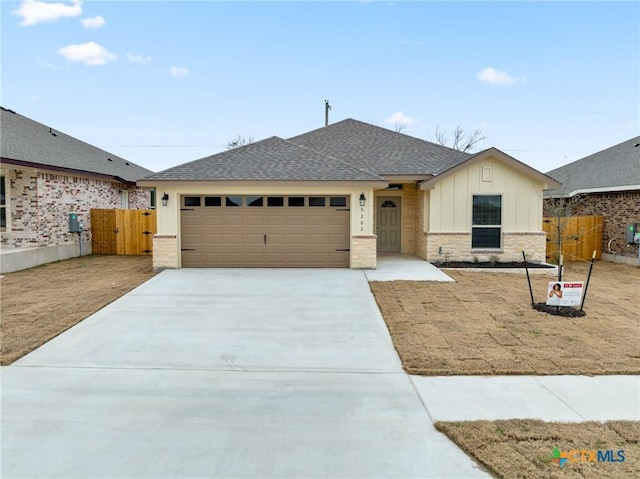 view of front facade with a shingled roof, concrete driveway, board and batten siding, fence, and a garage