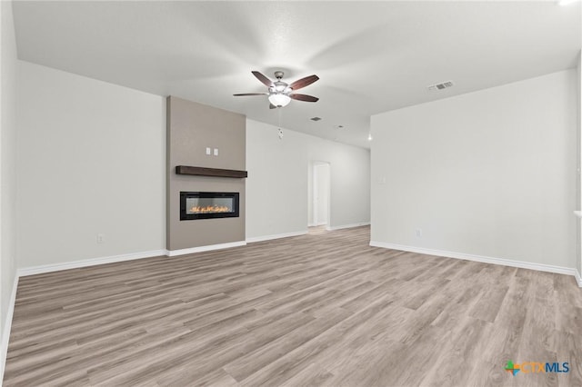 unfurnished living room featuring light wood-style flooring, visible vents, baseboards, and a glass covered fireplace