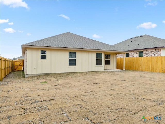 rear view of house with board and batten siding, roof with shingles, and a fenced backyard