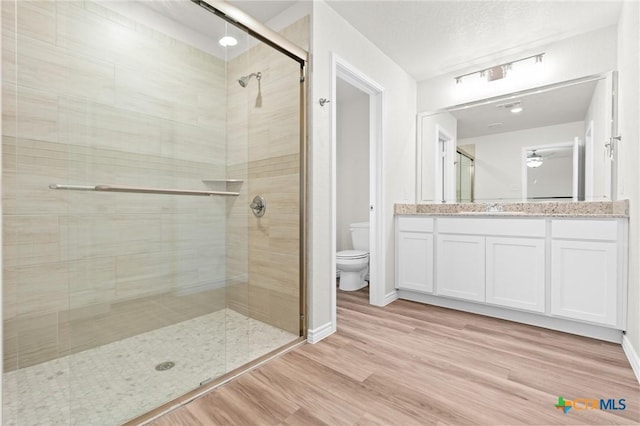 bathroom featuring toilet, a stall shower, vanity, wood finished floors, and baseboards