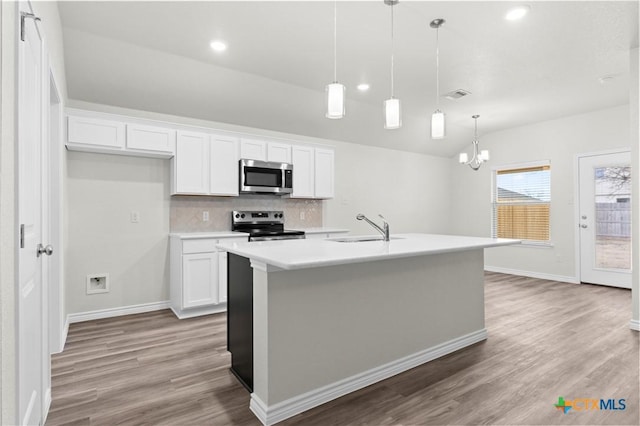 kitchen featuring stainless steel appliances, white cabinets, light countertops, an island with sink, and decorative light fixtures