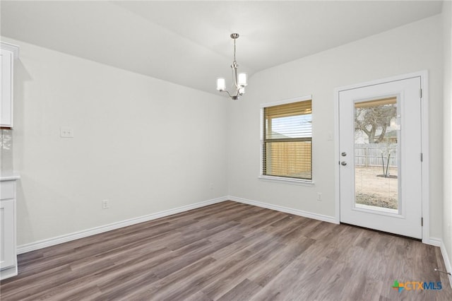 unfurnished dining area with lofted ceiling, a notable chandelier, baseboards, and wood finished floors