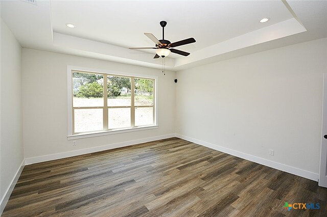 spare room featuring dark wood-type flooring, ceiling fan, and a raised ceiling