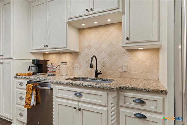 kitchen featuring white cabinetry, stainless steel dishwasher, sink, and light stone countertops