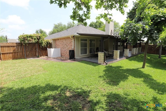 back of house featuring a patio, a chimney, a lawn, brick siding, and a fenced backyard