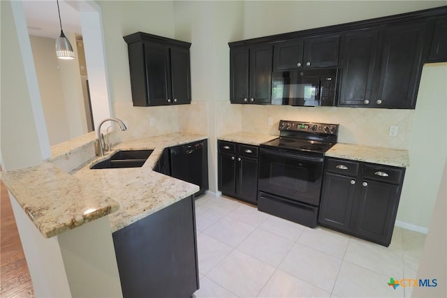 kitchen featuring light stone counters, a sink, black appliances, a peninsula, and dark cabinetry