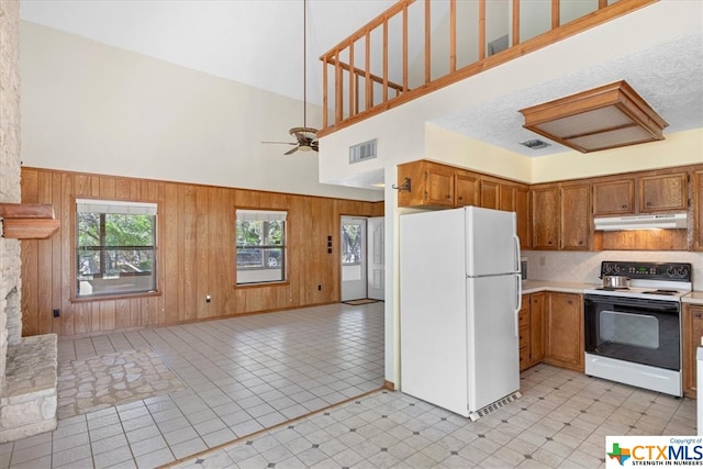 kitchen featuring a textured ceiling, wooden walls, ceiling fan, white appliances, and a high ceiling