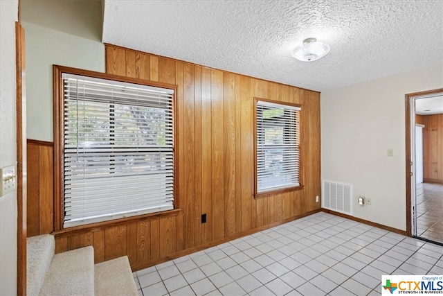 spare room featuring wood walls, light tile patterned flooring, and a textured ceiling