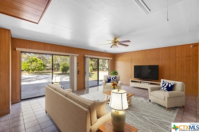 living room with wood walls, light tile patterned floors, and ceiling fan