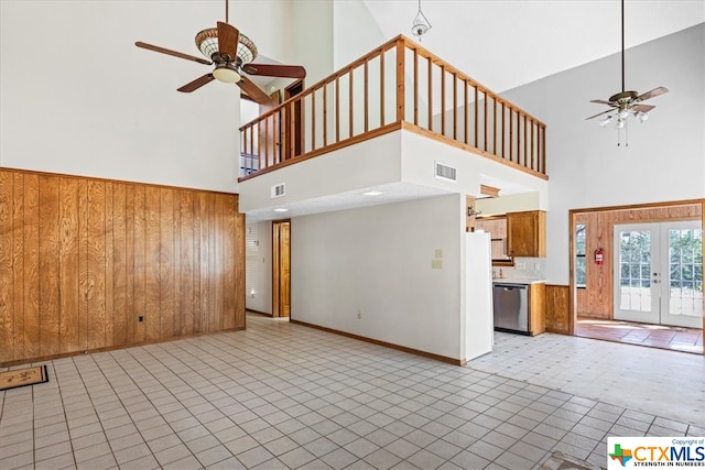 unfurnished living room featuring french doors, wood walls, ceiling fan, and a high ceiling