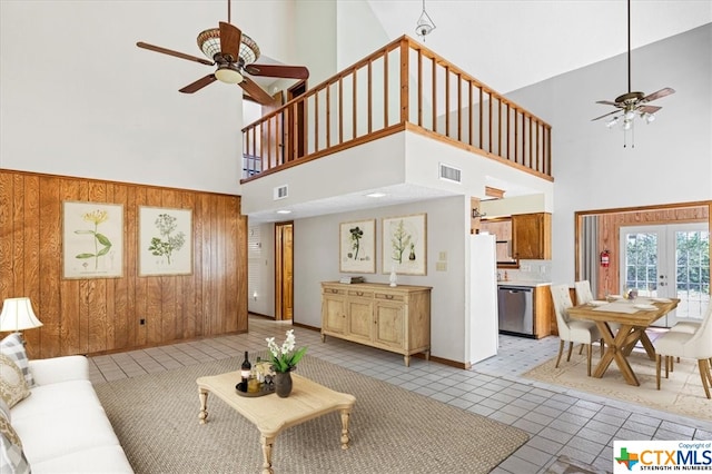 tiled living room featuring wood walls, a towering ceiling, ceiling fan, and french doors