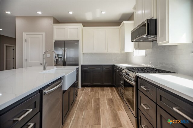 kitchen featuring light wood-type flooring, appliances with stainless steel finishes, light stone countertops, sink, and white cabinets