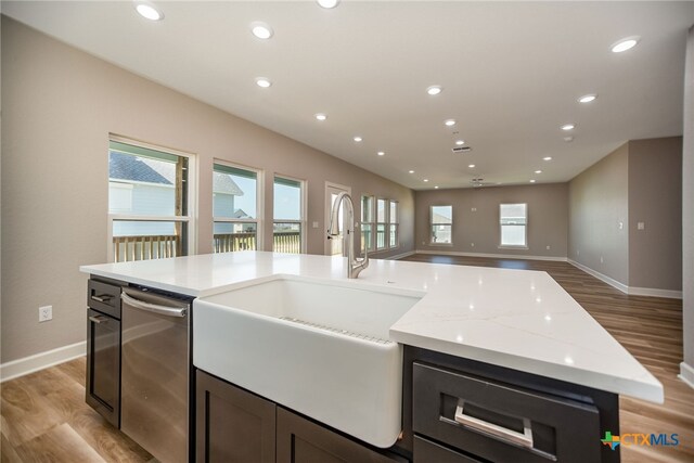 kitchen with light stone countertops, light hardwood / wood-style floors, a center island with sink, and a healthy amount of sunlight