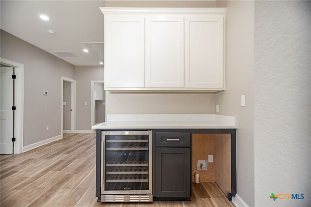 bar with white cabinets, light wood-type flooring, beverage cooler, and light stone countertops