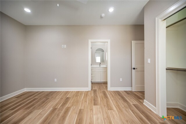 unfurnished bedroom featuring a closet, ensuite bath, sink, and light hardwood / wood-style flooring