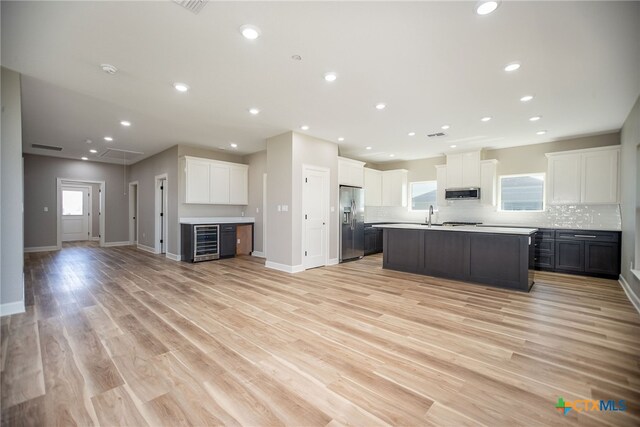 kitchen featuring tasteful backsplash, stainless steel appliances, light wood-type flooring, white cabinetry, and a kitchen island with sink