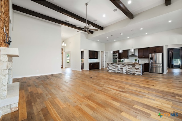 unfurnished living room with ceiling fan, light hardwood / wood-style floors, beamed ceiling, and a stone fireplace