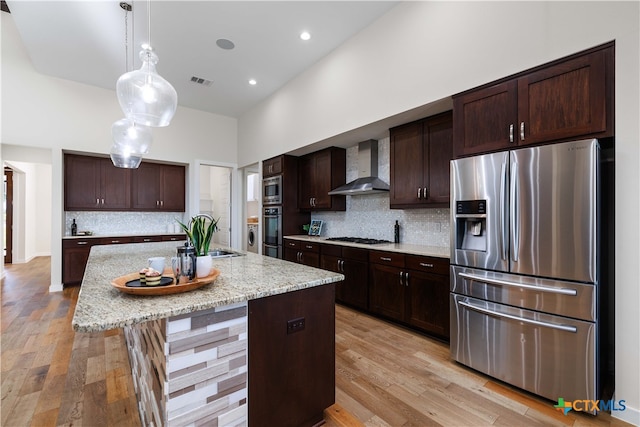 kitchen featuring stainless steel appliances, light hardwood / wood-style floors, wall chimney exhaust hood, an island with sink, and dark brown cabinets