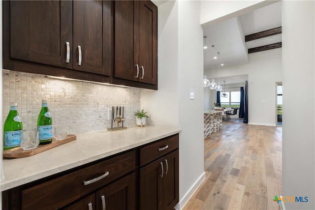 bar featuring light stone countertops, dark brown cabinets, beam ceiling, and light hardwood / wood-style flooring