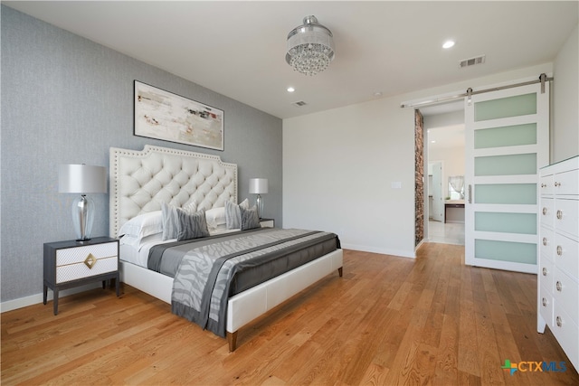 bedroom with a barn door and light wood-type flooring