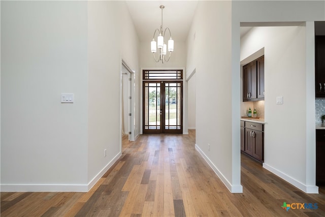 foyer with french doors, light wood-type flooring, a towering ceiling, and a chandelier